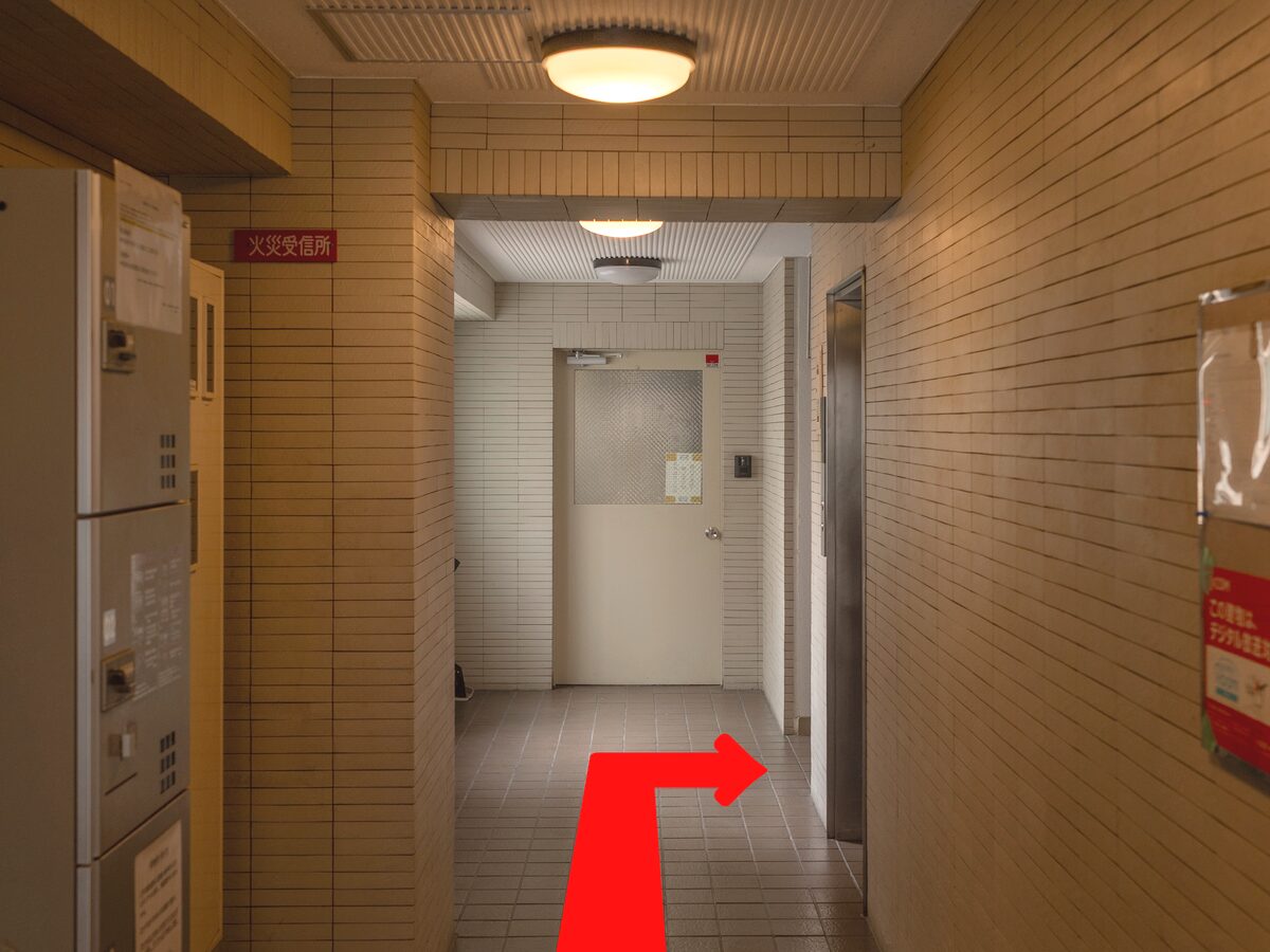 The hallway just inside the building, with mailboxes on the left. Turn right just before the white door at the end, as the red arrow shows.